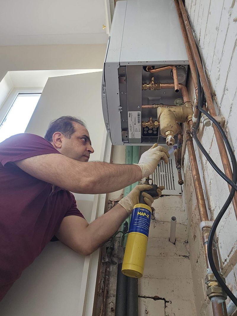 Engineer holding a blowtorch beneath a wall-hung boiler with a brass filter fitted