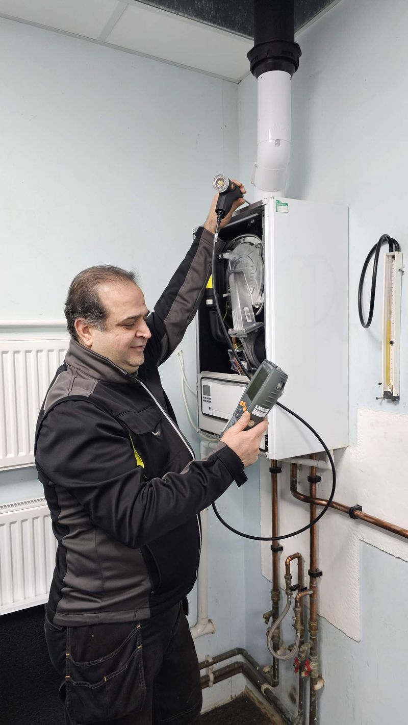 The engineer smiling while checking a wall-hung boiler with a flue gas analyser