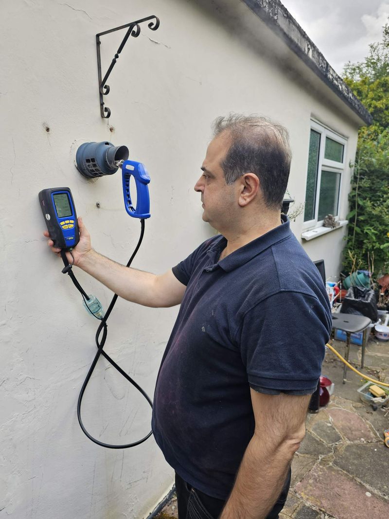 Engineer holding a flue gas analyser probe at a boiler's outside flue terminal