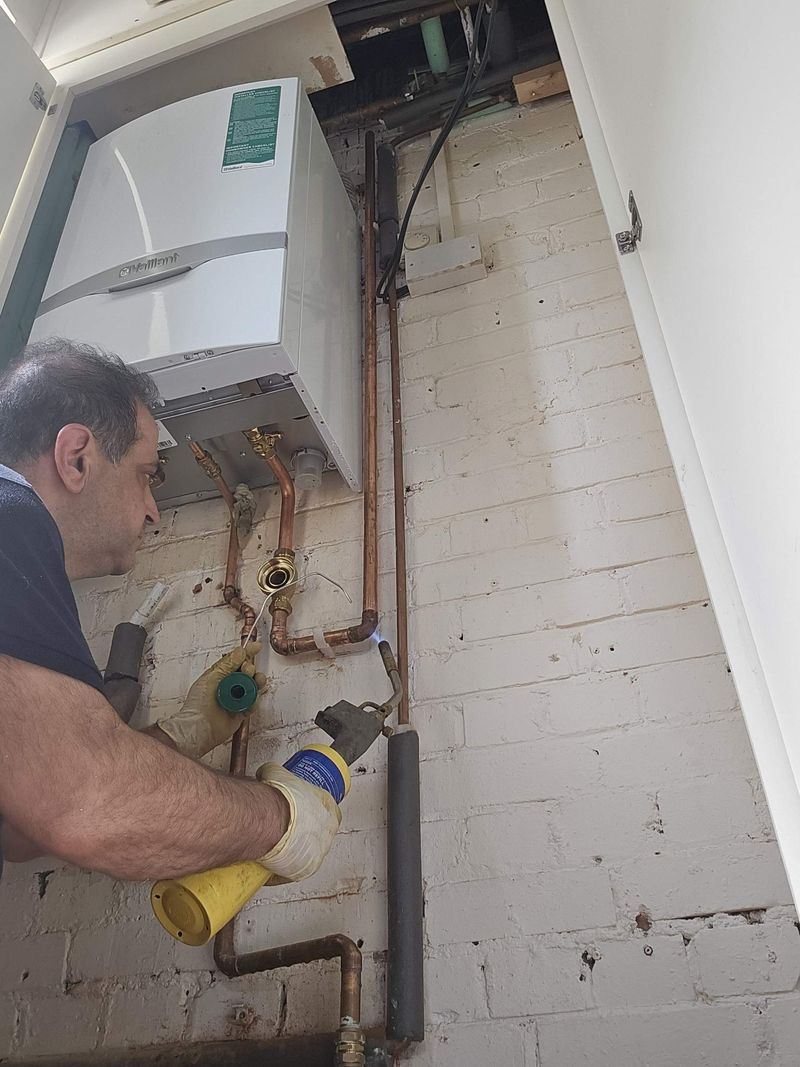 Engineer soldering copper pipework beneath a wall-hung Vaillant boiler
